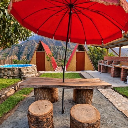 Finca Charritos: mesa rústica bajo sombrilla roja, piscina de piedra y cabañas en Santa Rosa de Quives